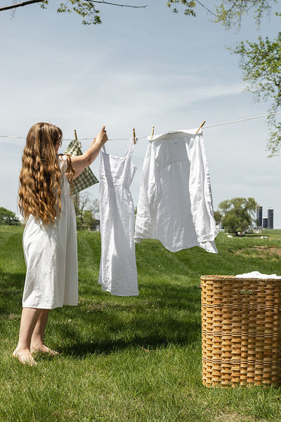 Woman hanging laundry on a clothesline in a grassy outdoor setting