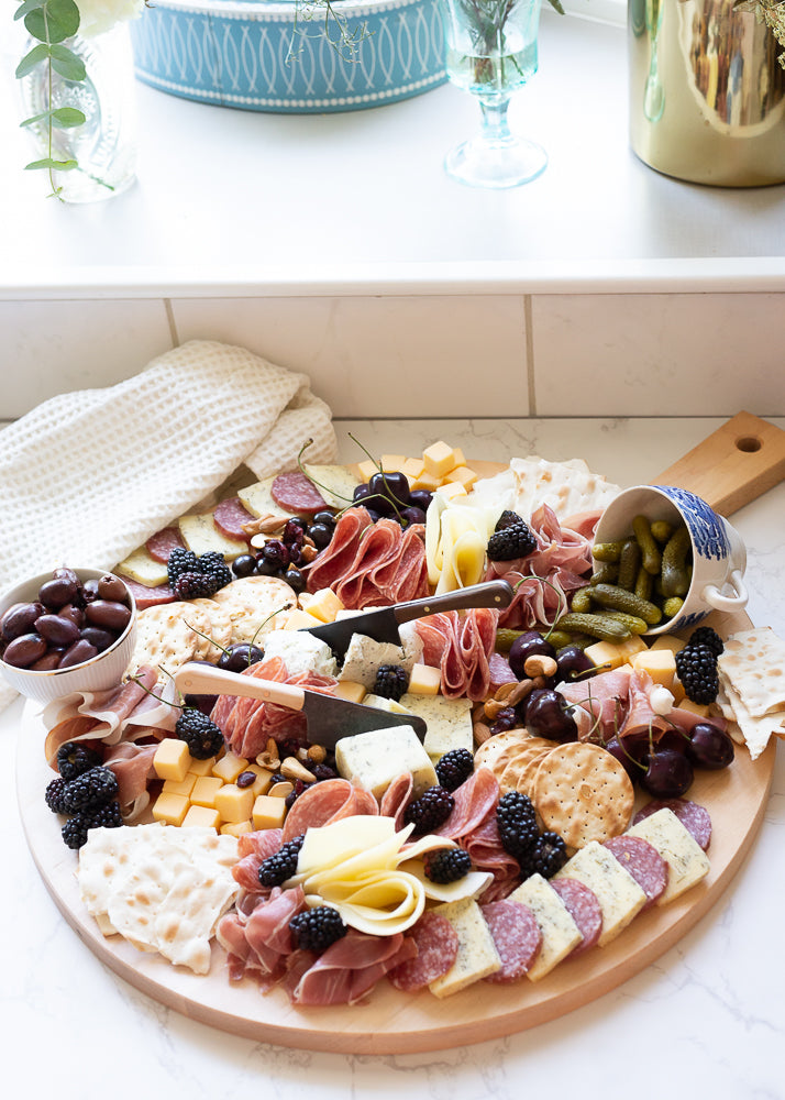 The Round Serving Board with Cheese, Crackers, and Other Foods on it