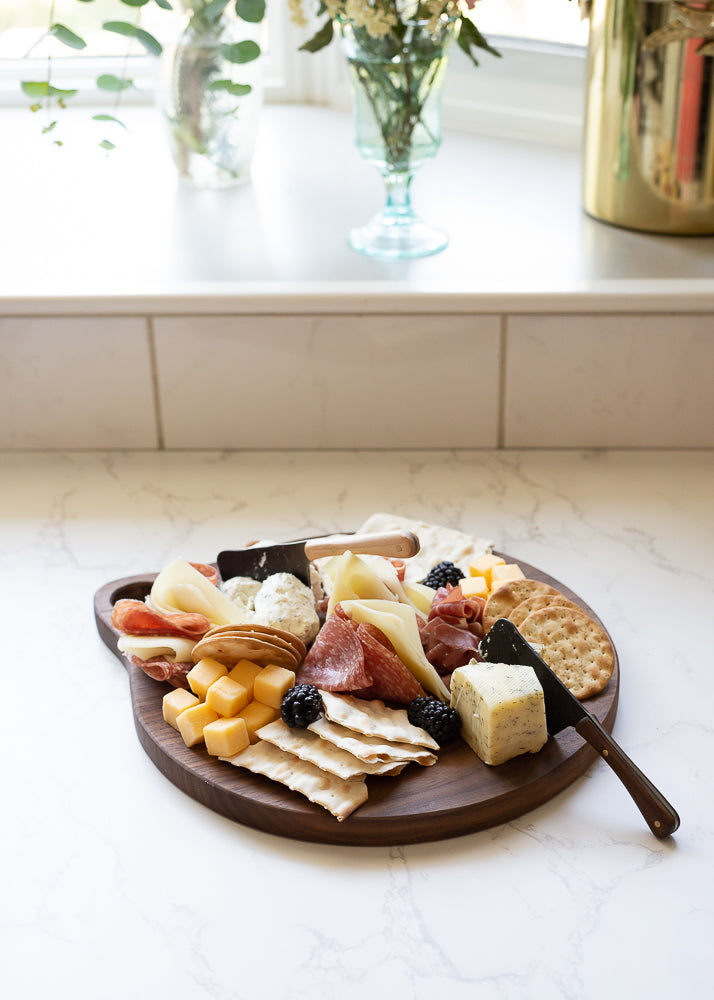 The Walnut Handcrafted Round Cutting Board with Assorted Cheeses and Crackers on Display